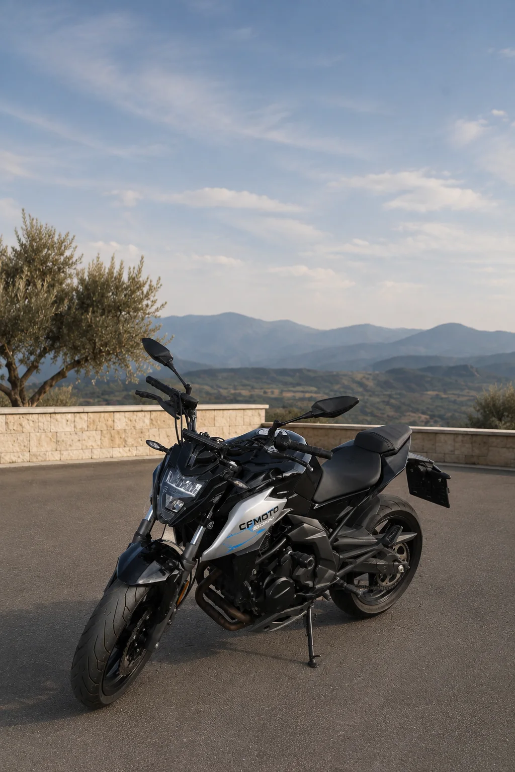 Siyah ve gri CFMOTO motosiklet, taş teras ve dağ manzarası önünde